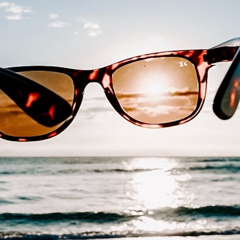 Ένα άτομο κρατάει ένα ζευγάρι γυαλιά ηλίου μπροστά από τη θάλασσα. 