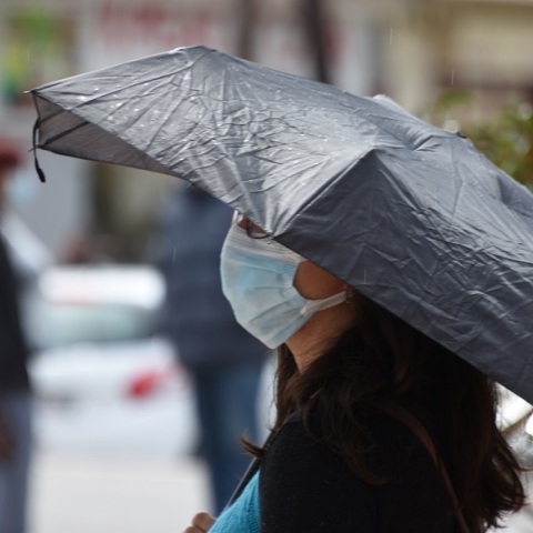 Βροχοπτώσεις - Γυναίκα που φορά μάσκα κρατά την ομπρέλα της