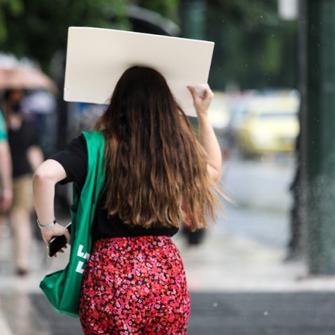 Καιρός: Νεαρή γυναίκα προσπαθεί να προστατευτεί από βροχόπτωση στην Αθήνα