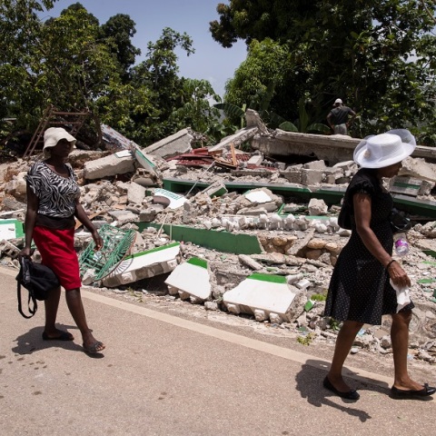 Σεισμός στην Αϊτή: Γυναίκες περπατούν δίπλα σε γκρεμισμένο κτίριο