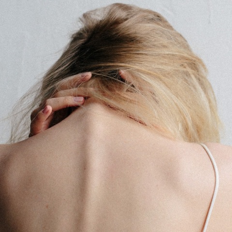 Γυναίκα με γυρισμένη πλάτη και σκυμμένο κεφάλι, κρατάει τον αυχένα της