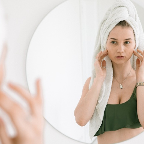 Κοπέλα κοιτάζεται σε καθρέφτη και ακουμπάει το πρόσωπό της