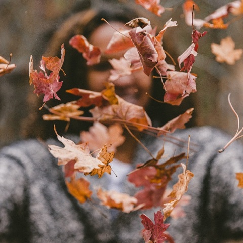 Ένα κορίτσι πετάει στον αέρα φθινοπωρινά φύλλα.