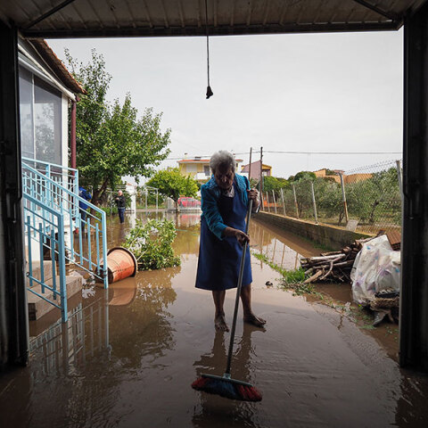 Πλημμύρες στη Βόρεια Εύβοια: Ηλικιωμένη με σκούπα απομακρύνει το νερό της βροχής που έφερε λάσπες και χώματα στο σπίτι της