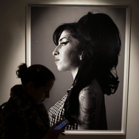 Γυναίκα κοιτά το smartphone της με φόντο πορτρέτο της Amy Winehouse
