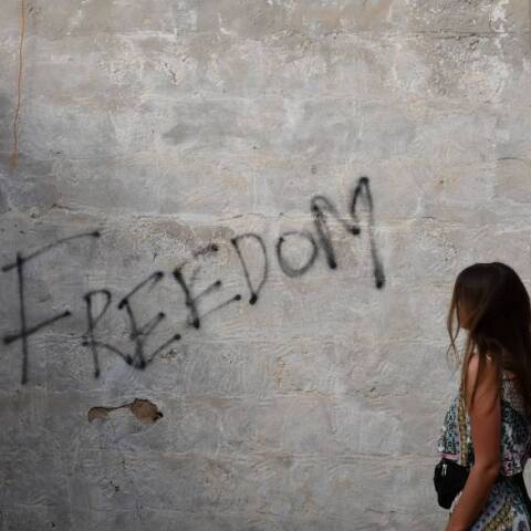 Γυναίκα κοιτάει έναν τοίχο όπου είναι γραμμένη η λέξη Freedom (Ελευθερία)