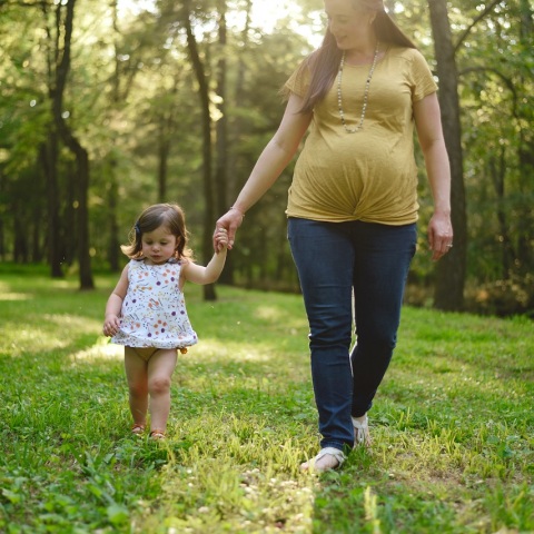 Έγκυος γυναίκα κρατάει από το χέρι μικρό κοριτσάκι σε δάσος
