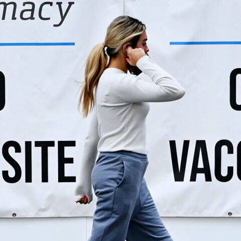 Κοπέλα στις ΗΠΑ μιλά στο κινητό, περνώντας μπροστά από αφίσες για τον εμβολιασμό κατά του κορωνοϊού