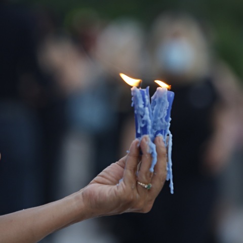 Γυναικείο χέρι που κρατά δύο αναμμένα κεριά σε εξωτερικό χώρο