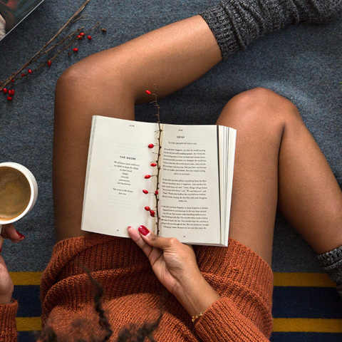 Μια κοπέλα καθισμένη με καφέ στο χέρι κι ένα βιβλίο στα πόδια της