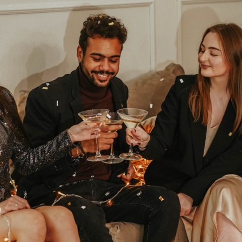 Τρεις φίλοι τσουγκρίζουν τα ποτά τους δίπλα από το χριστουγεννιάτικο δέντρο. 