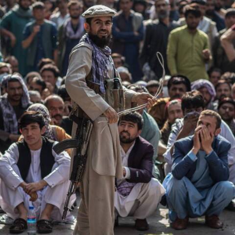 Ένας φρουρός ασφαλείας των Ταλιμπάν κρατάει μαστίγιο ενώ στέκεται μπροστά σε Αφγανούς άνδρες που περιμένουν έξω από μια τράπεζα για να βγάλουν χρήματα 