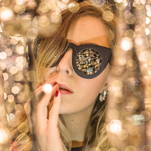 Γυναίκα με γυαλιά ηλίου ανάμεσα σε χρυσά χριστουγεννιάτικα λαμπάκια