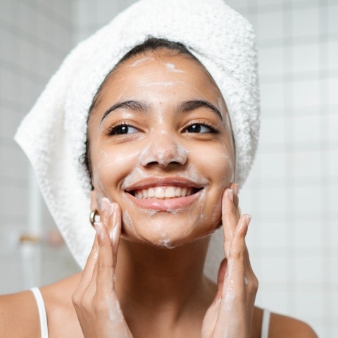 Κοπέλα με πετσέτα στα μαλλιά σαπουνίζει το πρόσωπό της