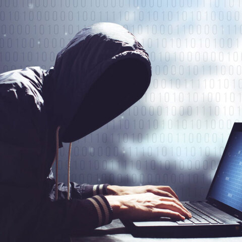 Άνθρωπος με κουκούλα και κρυμμένο πρόσωπο πληκτρολογεί σε υπολογιστή