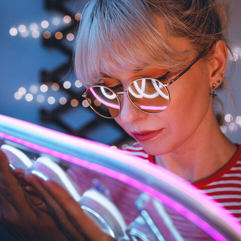 Κοπέλα με κοντά ηανθά μαλλιά κρατάει μια neon πινακίδα