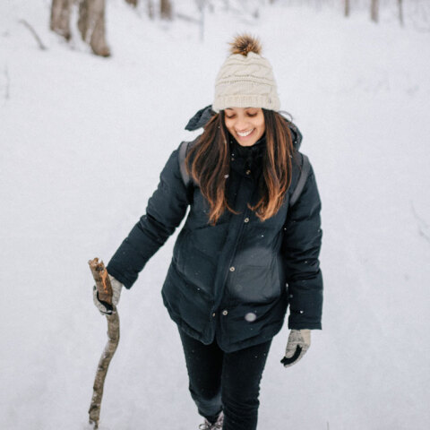 Κοπέλα με μαύρα ρούχα και λευκό σκουφάκι περπατάει στο χιόνι