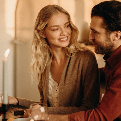 Γυναίκα και άνδρας κοιτάζονται καθισμένοι διπλα δίπλα σε τραπέζι με αναμμένα κεριά