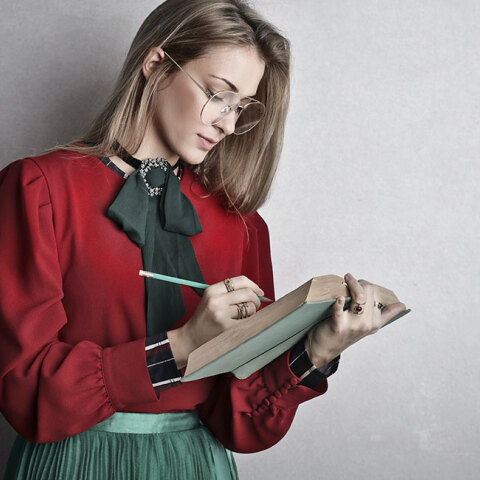 Νεαρή κοπέλα με πράσινη φούστα και κόκκινο πουκάμισο σημειώνει σε βιβλίο