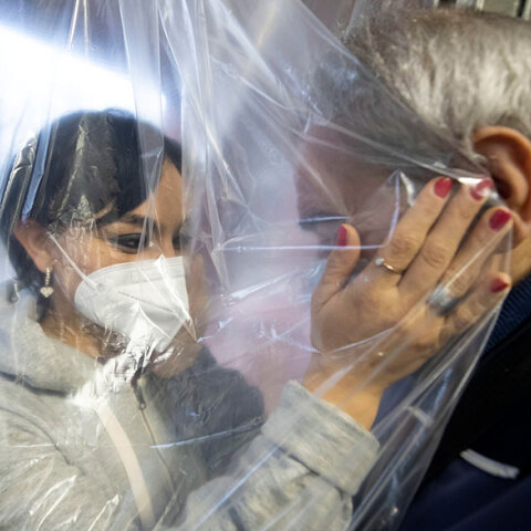 Γυναίκα με μάσκα στην Ιταλία αγκαλιάζει ηλικιωμένο σε γηροκομείο, έχοντας ανάμεσά τους μια ειδική πλαστική κουρτίνα