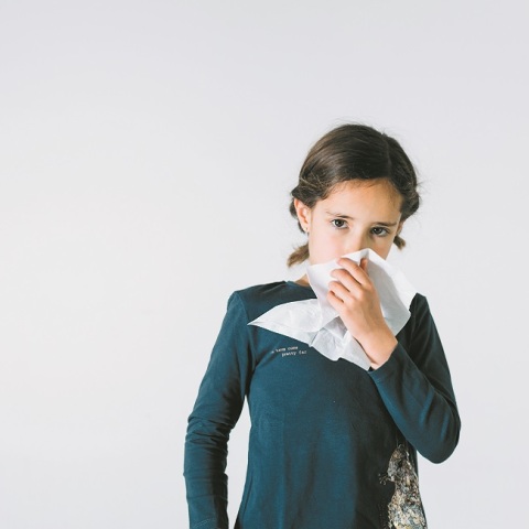 Ένα παιδί κρατάει ένα χαρτομάντηλο και κοιτάει την κάμερα. 