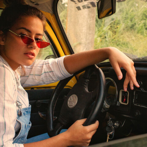Γυναίκα καθισμένη σε αυτοκίνητο, κρατάει τιμόνι και κοιτάζει την κάμερα