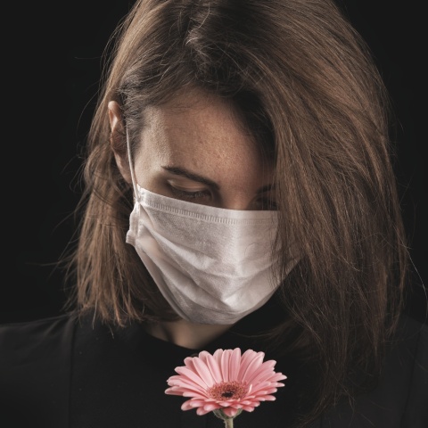 Γυναικά με μάσκα κρατά στα χέρια της ένα λουλούδι