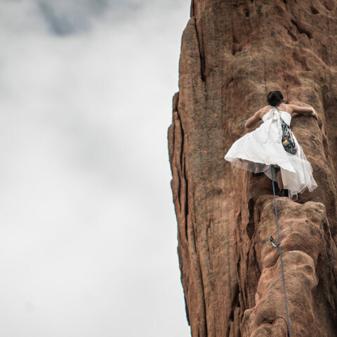 Γυναίκα με λευκό φόρεμα σκαρφαλώνει σε κάθετο βράχο