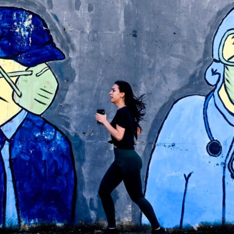Κοπέλα κάνει τζόκινγκ, περνώντας μπροστά από mural για τον κορωνοϊό