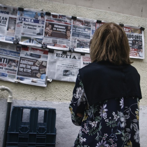 Γυναίκα διαβάζει τα πρωτοσέλιδα των εφημερίδων που βρίσκονται αναρτημένα σε περίπτερο