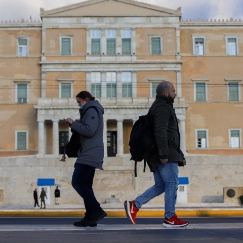 Άνδρας και Γυναίκα περπατούν στο κέντρο της Αθήνας με φόντο τη Βουλή των Ελλήνων