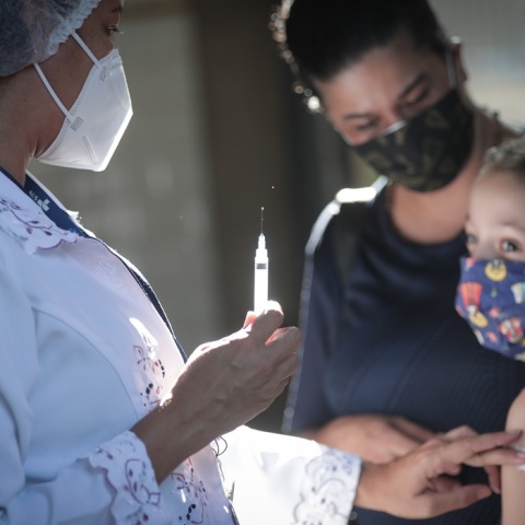 Παιδί στην αγκαλιά του γονέα του κοιτά το εμβόλιο κατά του κορωνοϊού λίγο πριν το κάνει η νοσηλεύτρια