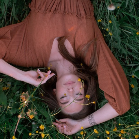 Ένα κορίτσι ξαπλώνει στο γρασίδι και ποζάρει. 