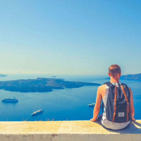 Άνδρας με σακίδιο πλάτης καθισμένος σε πεζούλι με φόντο τη θάλασσα