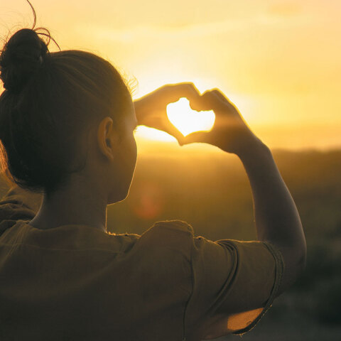 Κορίτσι σχηματίζει καρδιά με τα χέρια της με φόντο το ηλιοβασίλεμα