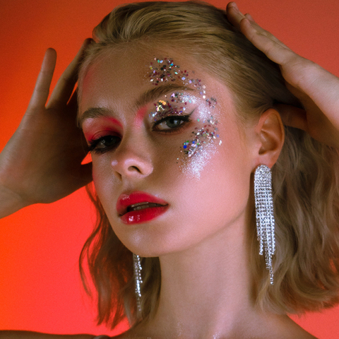 Κοπέλα με ξανθό καρέ μαλλί και στρας στο πρόσωπο που πιάνει το κεφάλι της