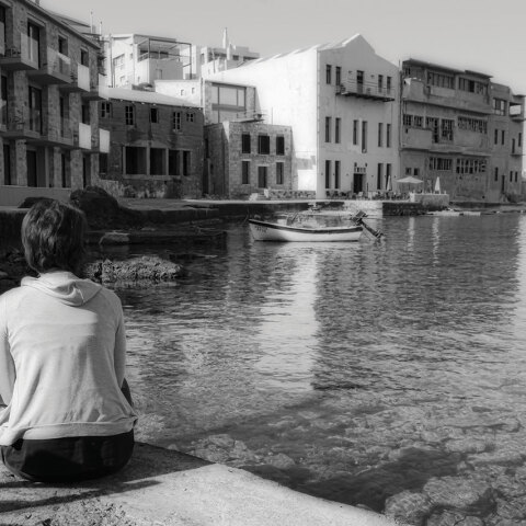 Ασπρόμαυρη φωτογραφία γυναίκας καθισμένης με γυρισμένη την πλάτη και φόντο τη θάλασσα