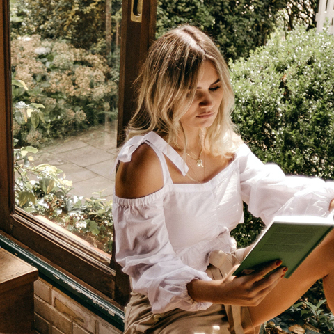 Μια κοπέλα κάθεται στο παράθυρο και διαβάζει ένα βιβλίο