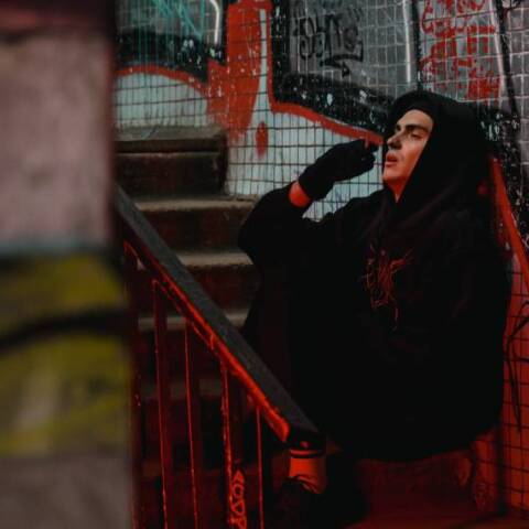 Άντρας με μαύρο φούτερ, κάθεται στα σκαλιά και καπνίζει