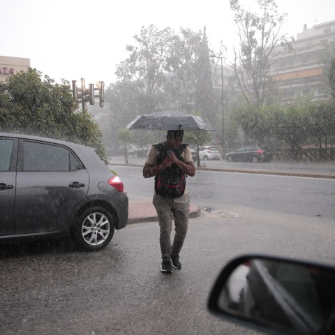Άντρας με ομπρέλα περπατάει κατά τη διάρκεια έντονης βροχόπτωσης στην Αθήνα