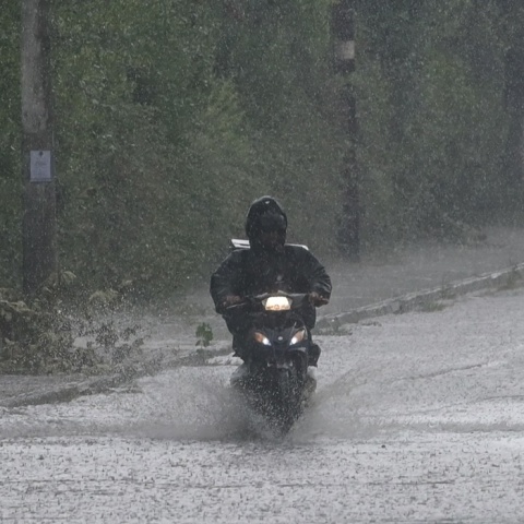 Κακοκαιρία: Διανομέας με αδιάβροχο οδηγεί μηχανάκι υπό καταρρακτώδη βροχή σε πλημμυρισμένο δρόμο