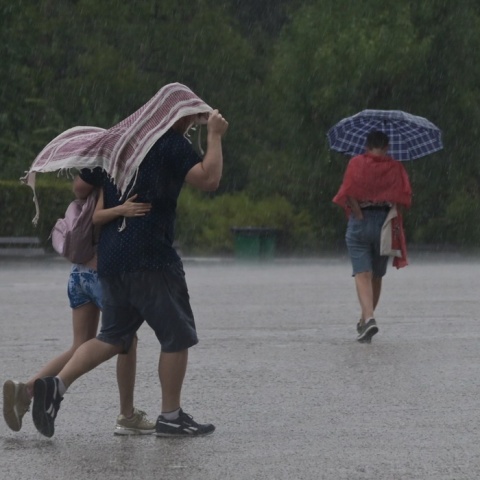 Πολίτες προστατεύονται από τη βροχή με πανωφόρι ή ομπρέλα