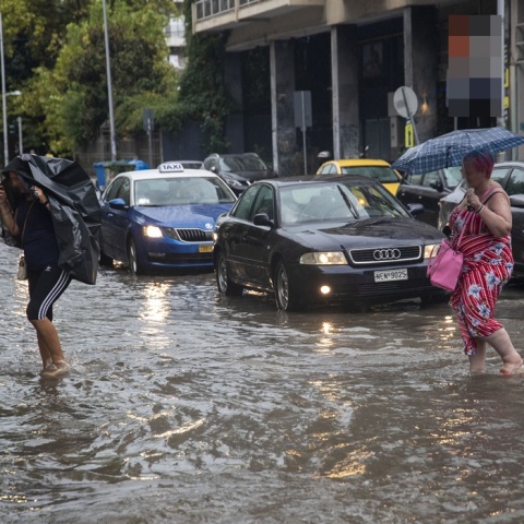 Πολίτες προσπαθούν να περάσουν πλημμυρισμένο δρόμο στη Θεσσαλονίκη και να προστατευτούν από τη βροχή