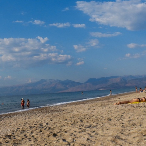 Λουόμενοι απολαμβάνουν τον ήλιο σε παραλία - Λίγα σύννεφα στον ουρανό