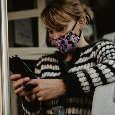Γυναίκα με μάσκα κοιτάζει το κινητό της