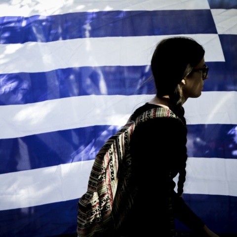 Γυναίκα προχωρά μπροστά από ελληνική σημαία που κυματίζει