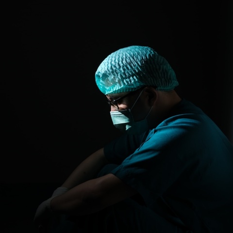 Γιατρός κουρασμένος φορά μάσκα και στέκεται στο ημίφως