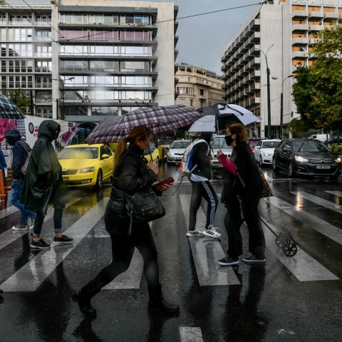 Πολίτες με ομπρέλα προστατεύονται από τη βροχή ενώ περπατούν σε δρόμο του κέντρου της Αθήνας