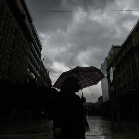 Πολίτης κρατά ομπρέλα για να προστατευτεί από τη βροχή σε σκοτεινιασμένο ουρανό