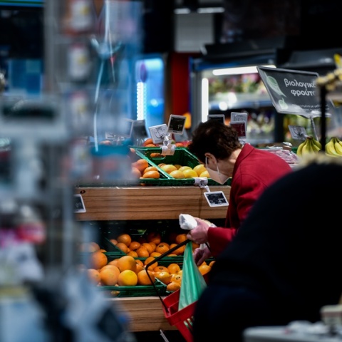 Γυναίκα ψωνίζει σε σούπερ μάρκετ φρούτα κρατώντας ένα κόκκινο καλάθι